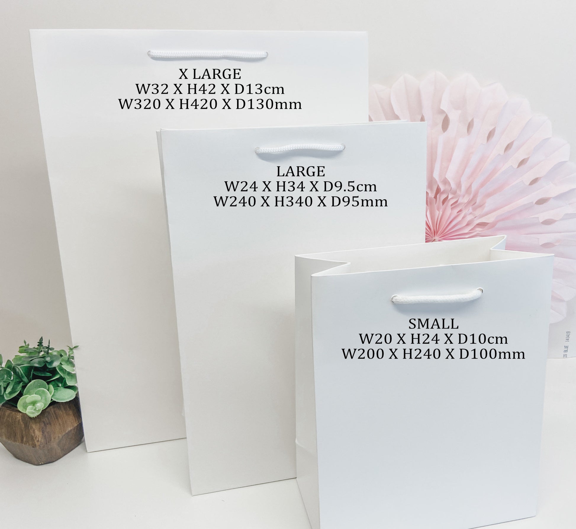 three white paper bags of different sizes, with a pink paper fan visible in the background.